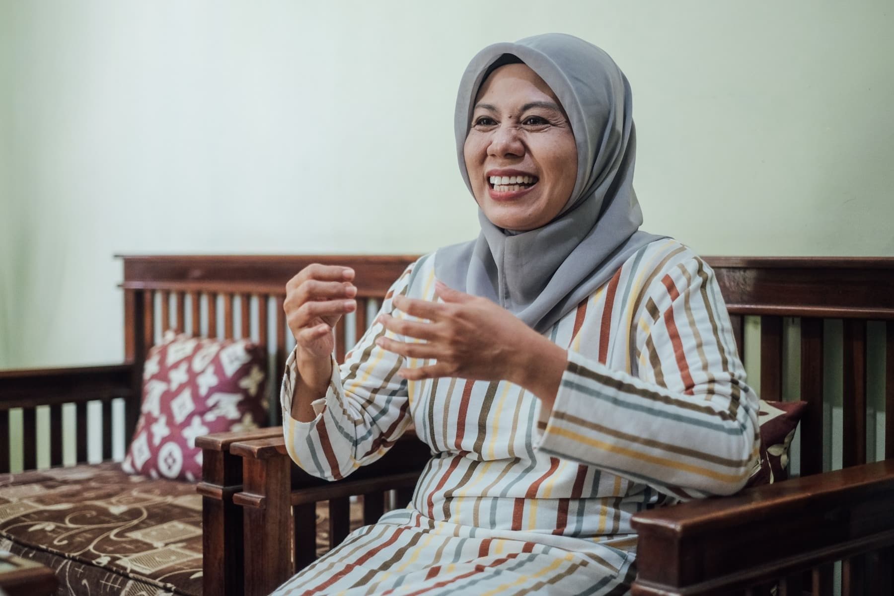 Foto Ibu Ririn sedang berbicara sembari tertawa dan menggunakan gesture tangan.