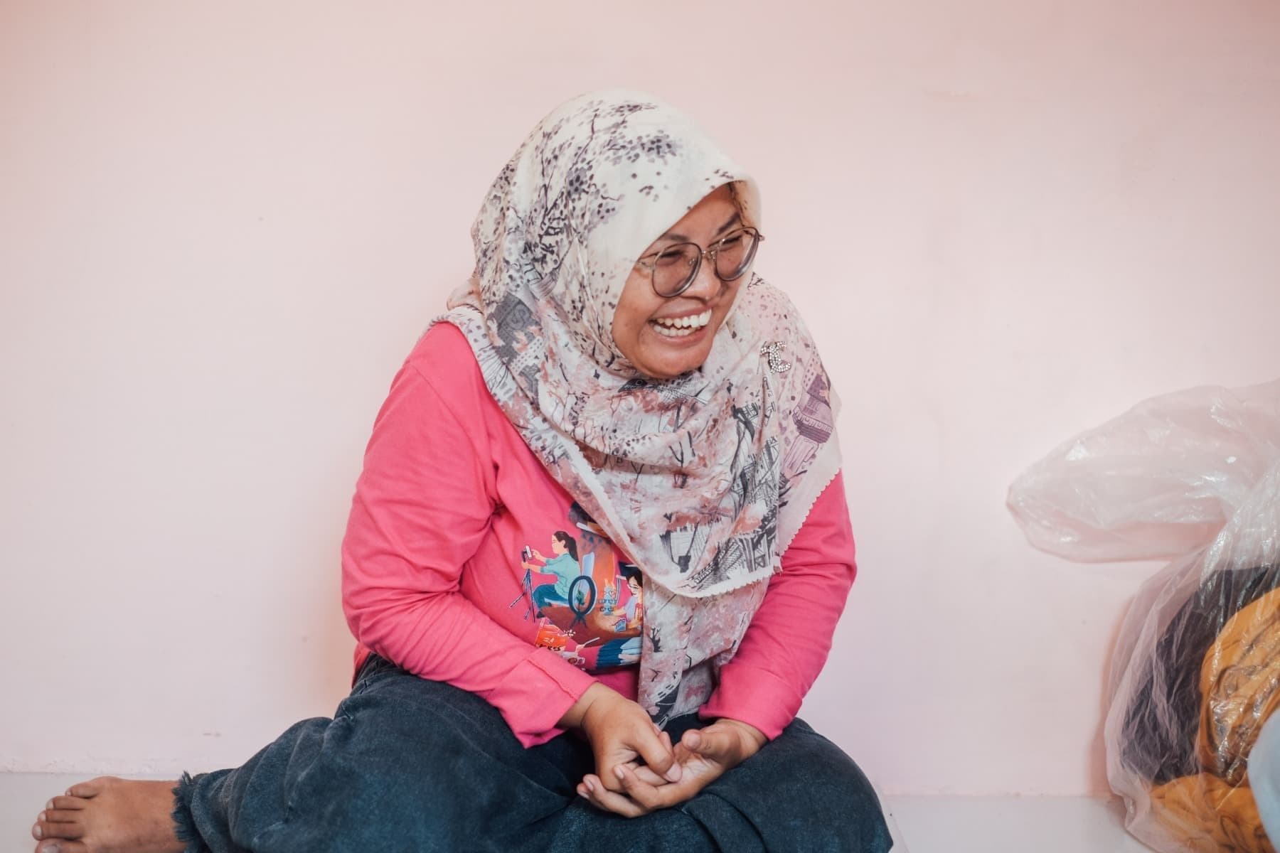 Foto Ibu Rani sedang tertawa lepas sembari terduduk.