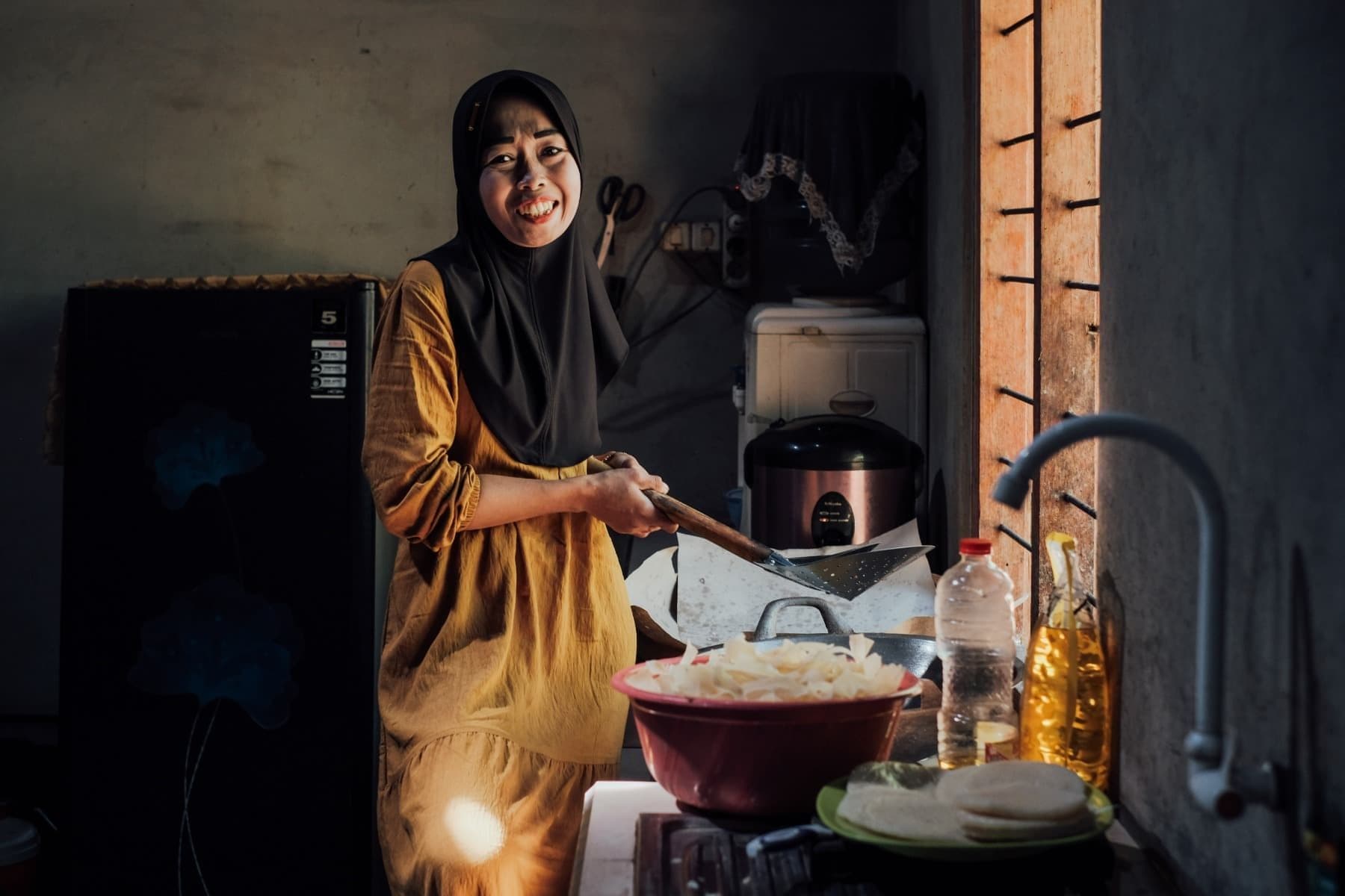 Foto Ibu Dita sedang tertawa sembari menggoreng keripik gatot.
